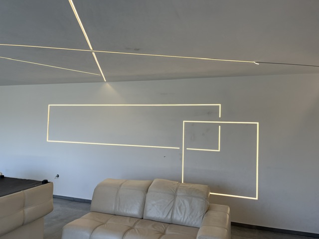 Geometrijska LED kompozicija na stropu i zidu iznad kožne garniture